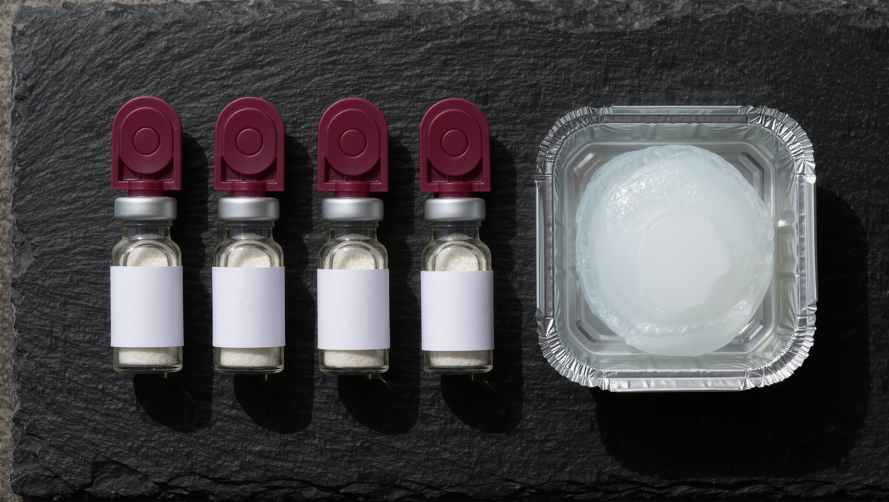Four maroon-capped peptide vials and an ice pack on slate, seen from above